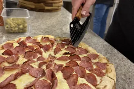 Pizza de pepperoni sendo cortada na bancada