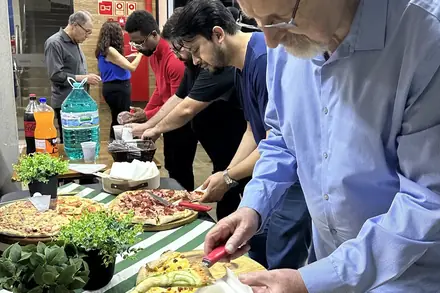 Convidado se servindo na mesa de pizzas da confraternização