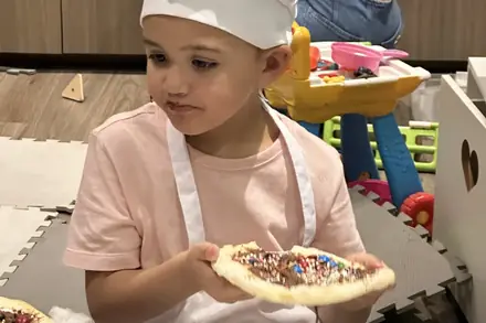 Criança de avental e chapéu de cozinheiro mostrando a pizza doce que decorou no Mini Chef