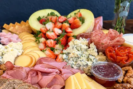 Mesa de frios com queijos fatiados, morangos e pão australiano