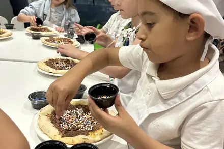 Crianças de chapéu de cozinheiro montando a pizza doce