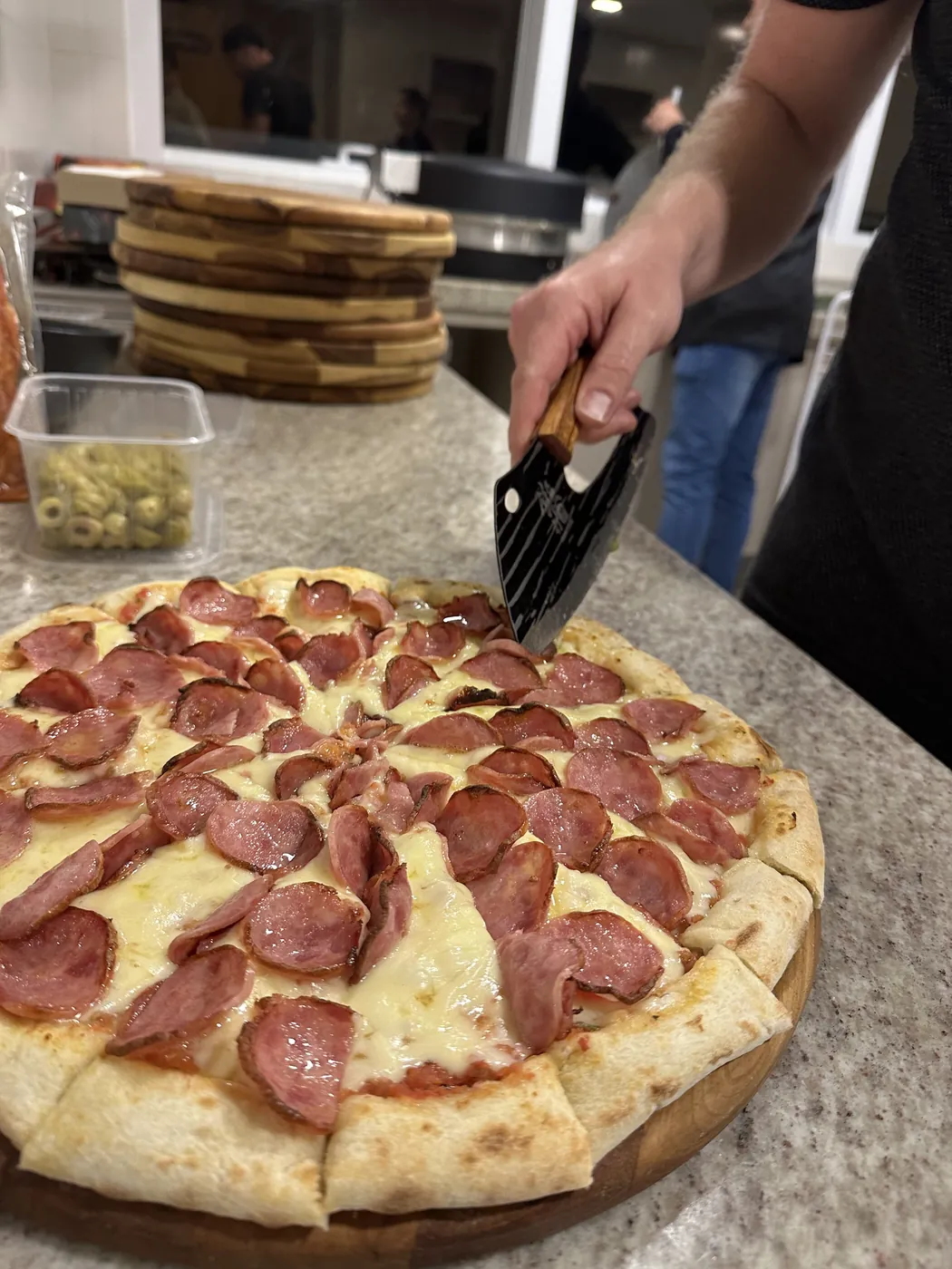 Pizza de pepperoni sendo cortada na bancada