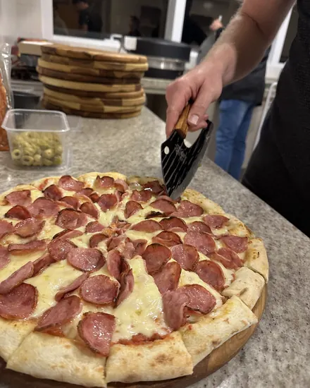 Pizza de pepperoni sendo cortada na bancada