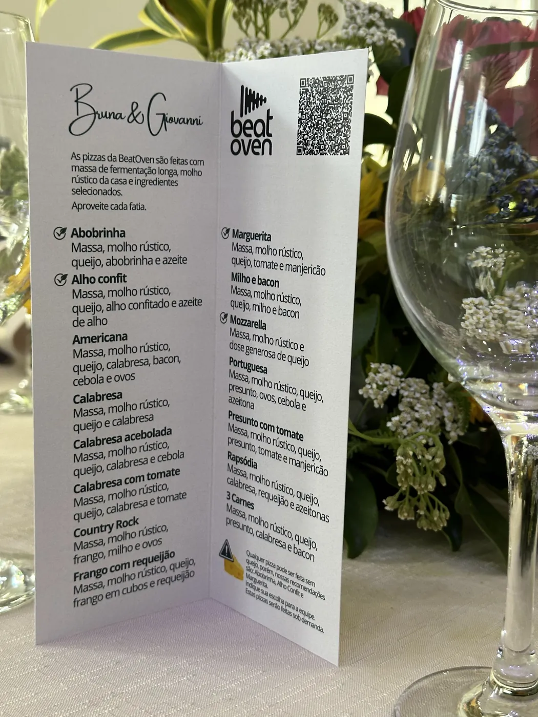 Cardápio impresso com o nome dos noivos e os sabores da noite, na mesa do casamento