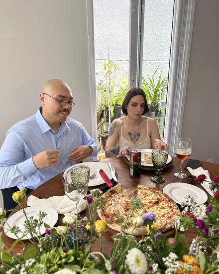 Os noivos à mesa decorada com flores, com a pizza servida