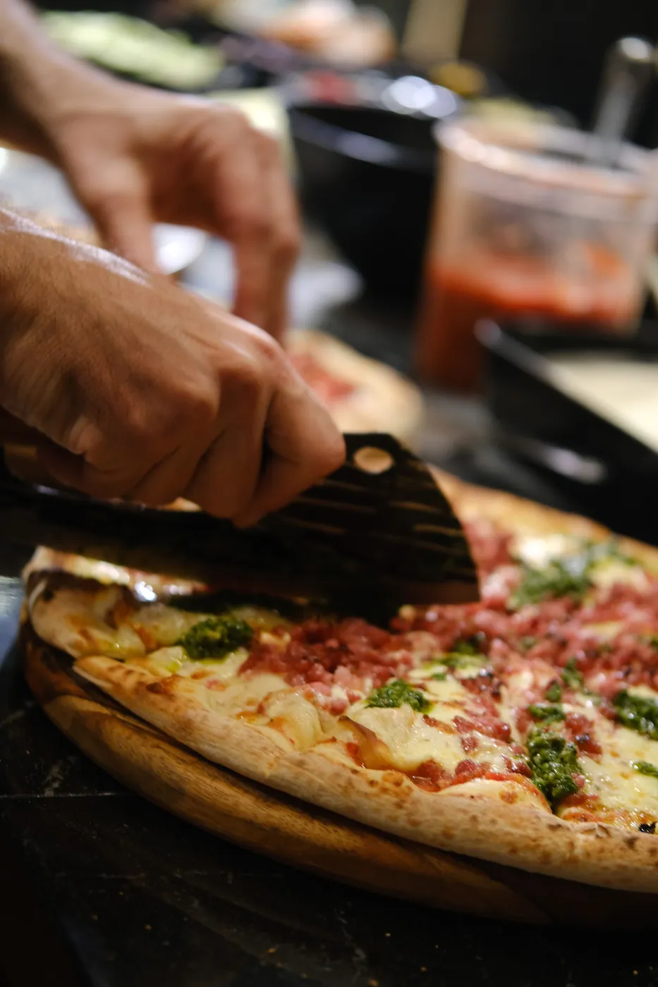 Pizza de calabresa com pesto sendo cortada na tábua