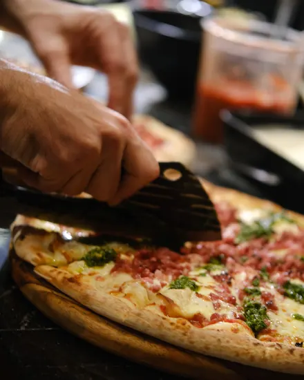 Pizza de calabresa com pesto sendo cortada na tábua