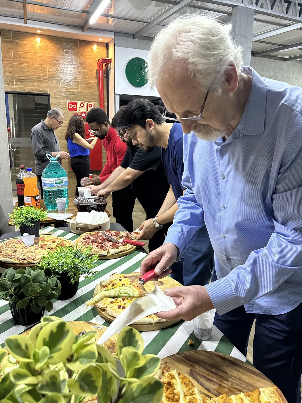 Convidado se servindo na mesa de pizzas da confraternização