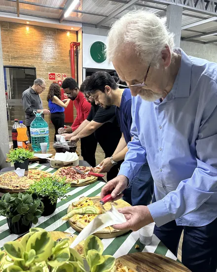 Convidado se servindo na mesa de pizzas da confraternização