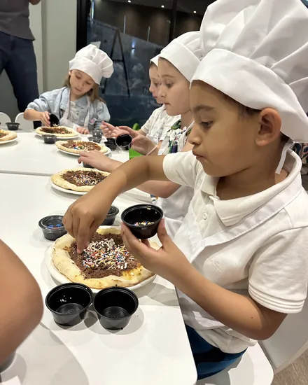 Crianças de chapéu de cozinheiro decorando a própria pizza doce no Mini Chef