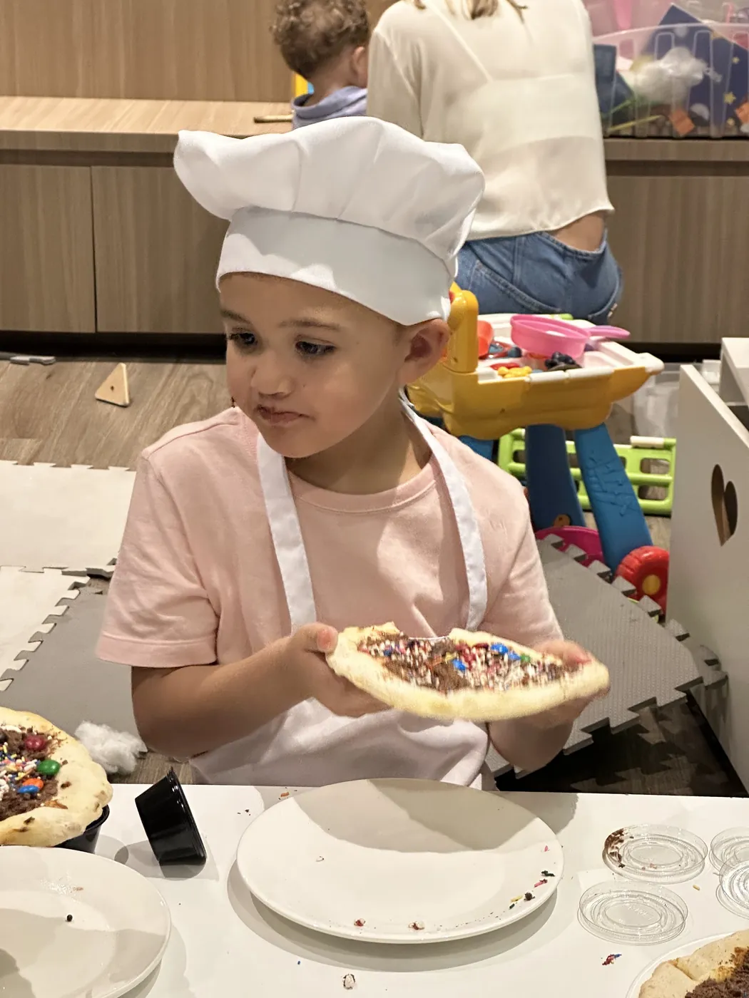 Criança de avental e chapéu de cozinheiro mostrando a pizza doce que decorou no Mini Chef