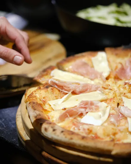 Tábua com a pizza recém-saída do forno indo para a mesa dos convidados