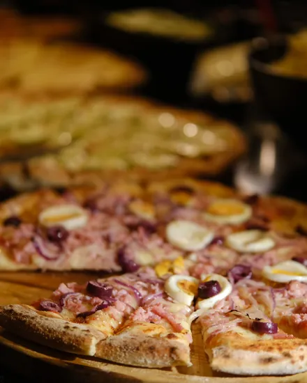 Pizza de presunto com ovos e cebola roxa servida na tábua