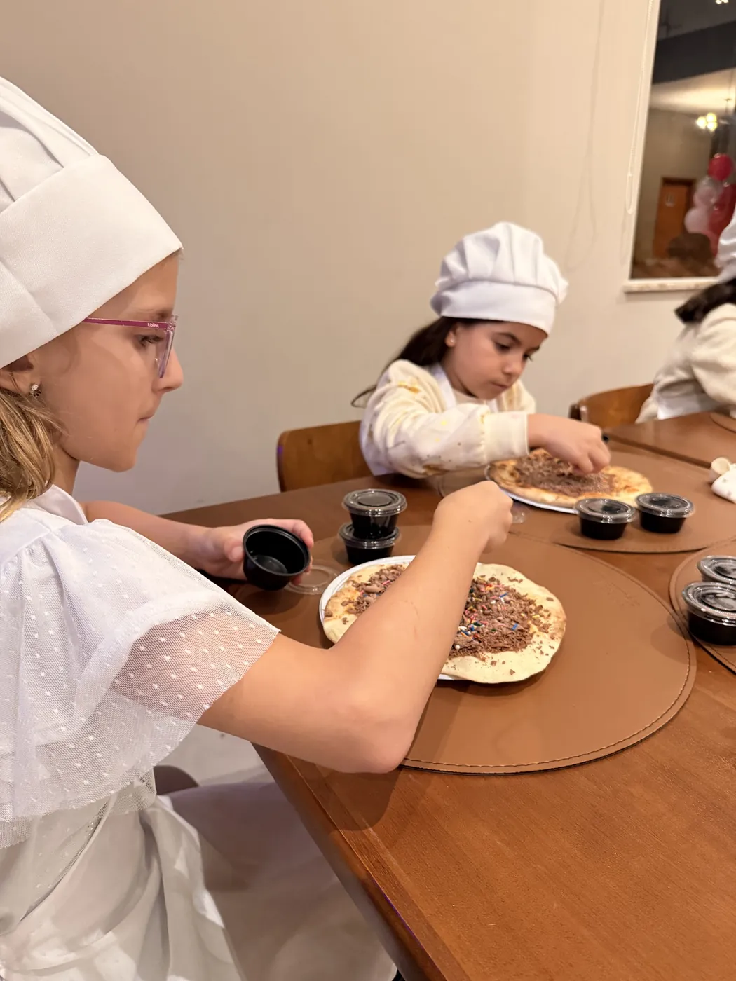 Criança de chapéu de cozinheiro decorando a pizza doce