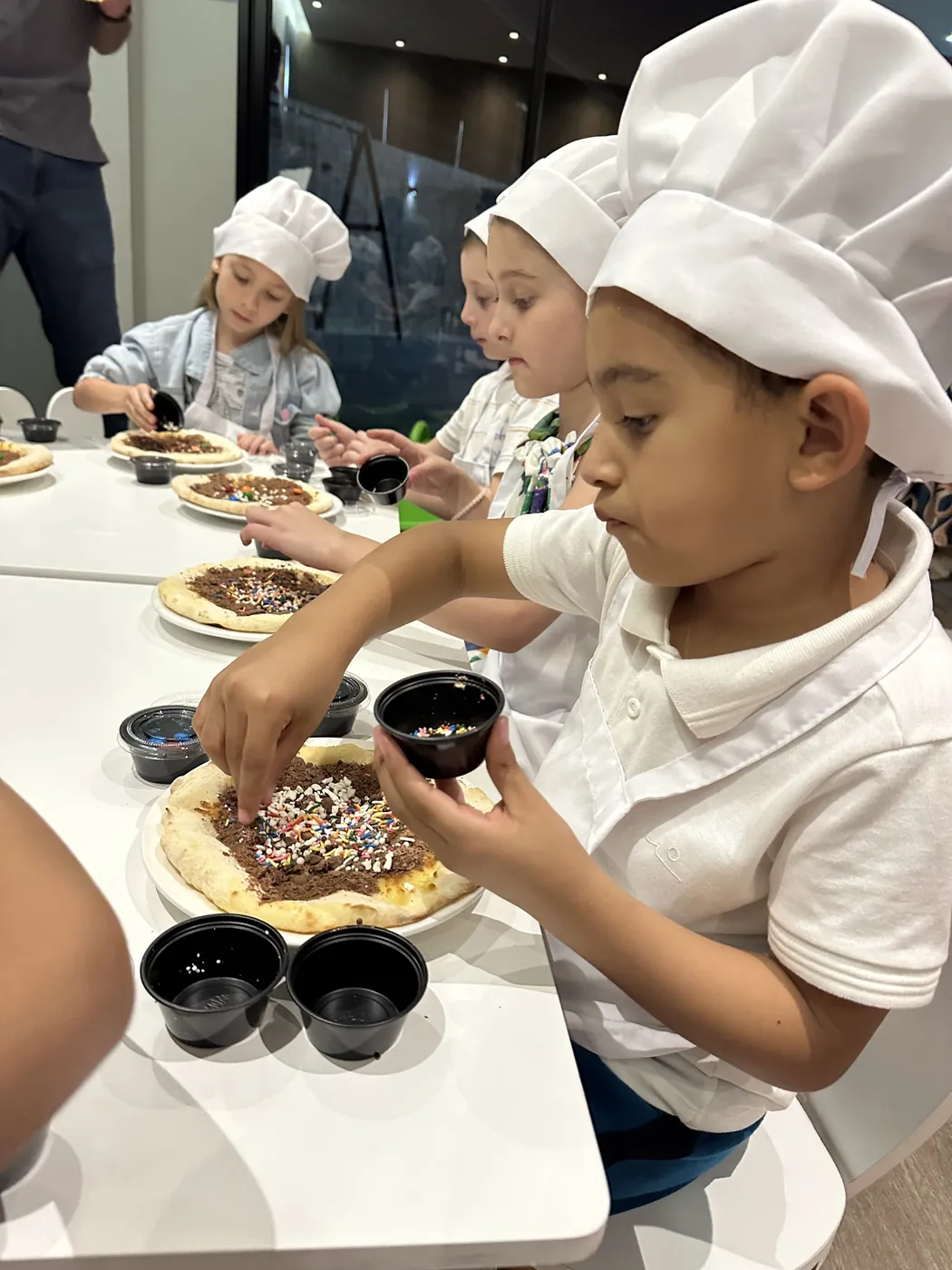Crianças de chapéu de cozinheiro montando a pizza doce
