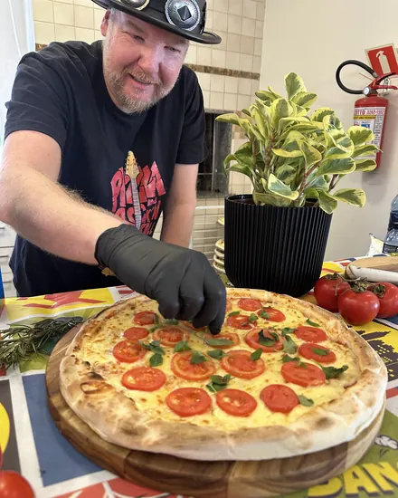Pizzaiolo da BeatOven finalizando a marguerita sobre a toalha temática da festa