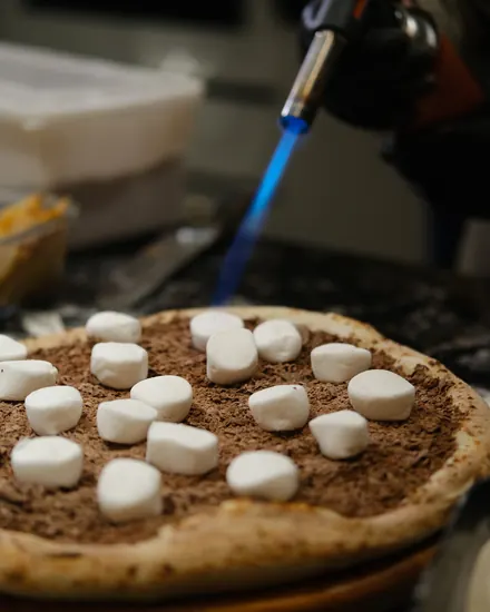 Pizza doce de chocolate com marshmallow sendo finalizada no maçarico