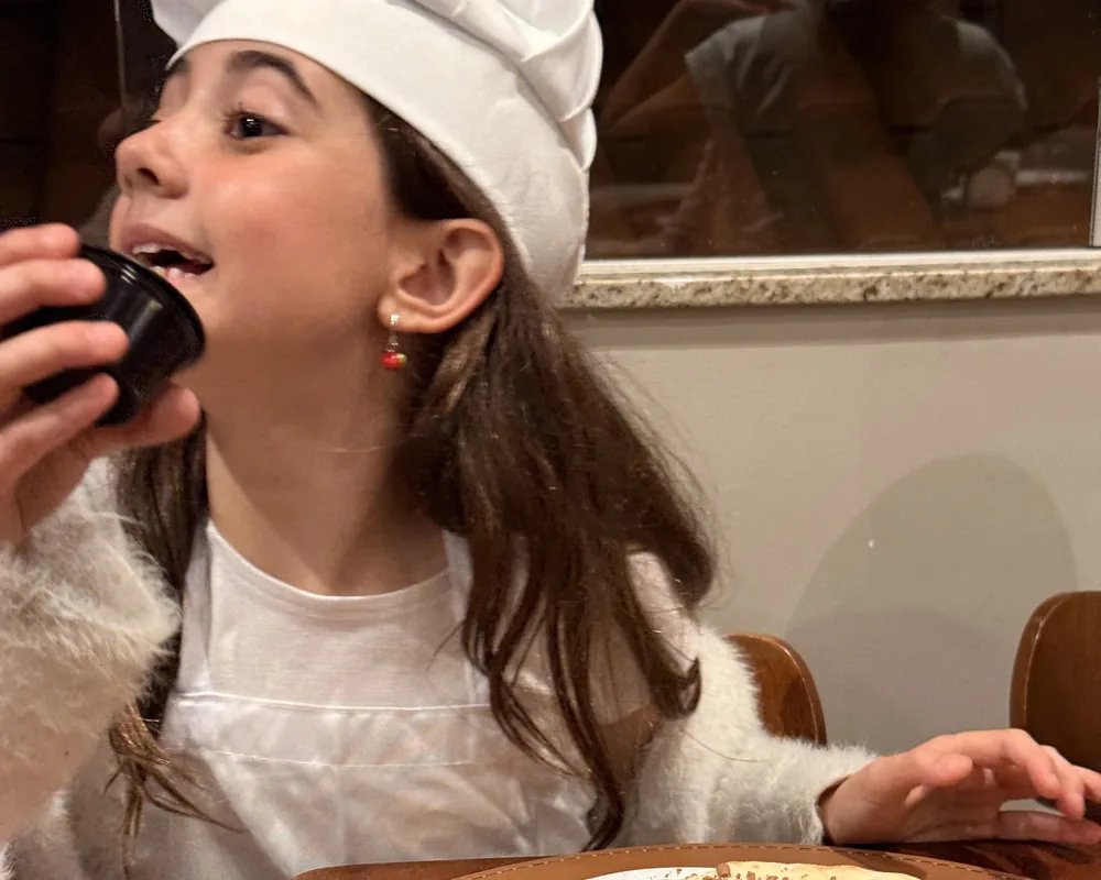 Criança de chapéu de cozinheiro provando a pizza doce que decorou no Mini Chef
