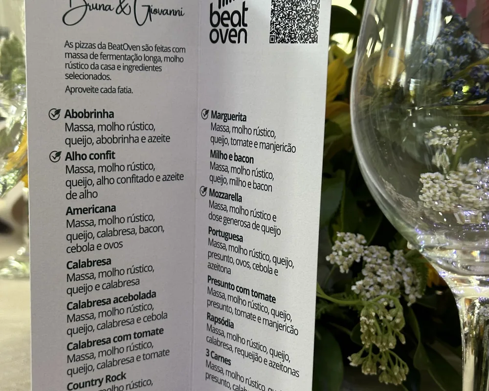 Cardápio impresso com o nome dos noivos, Bruna e Giovani, e os sabores da noite, na mesa do casamento